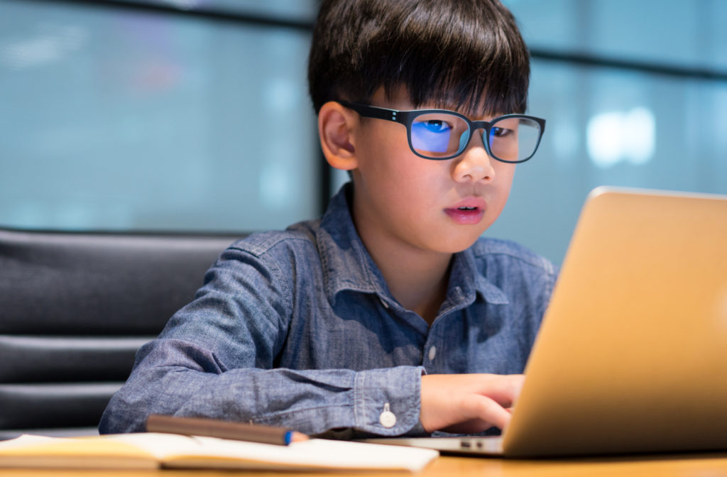 Young boy wearing blue light glasses while using laptop