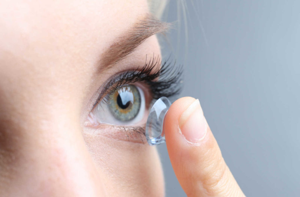 A close up of a woman holding a contact lens on her finger about to place it in her eye.