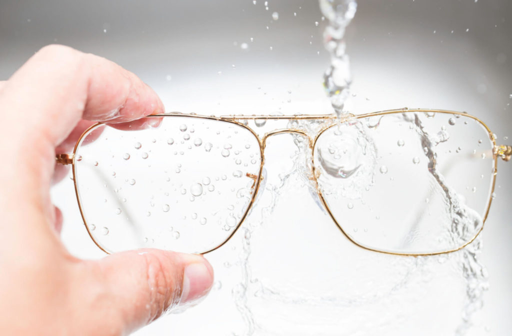 A man's hand washing his gold frame eye glasses into running water.