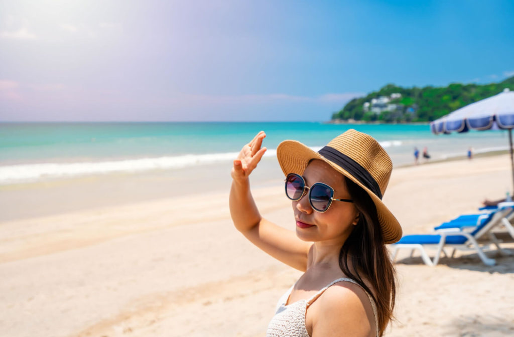 A woman is wearing UV-protective sunglasses to shield her eyes from UV radiation while she is at the beach.