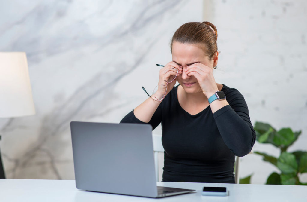 A woman rubbing her dry eyes due to a long time working in front of her computer screen.