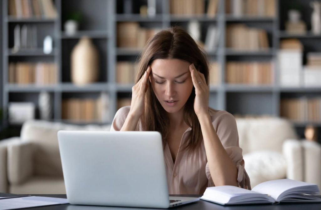 A woman is suffering from a headache after computer work due to eye strain. Using blue light-reducing or blocking glasses may help you cope with digital eye strain.