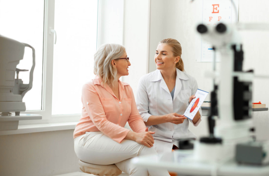 A senior woman sitting in an optometrist's office and smiling at her eye doctor.