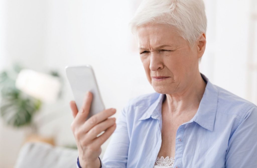An senior woman squinting at her phone.
