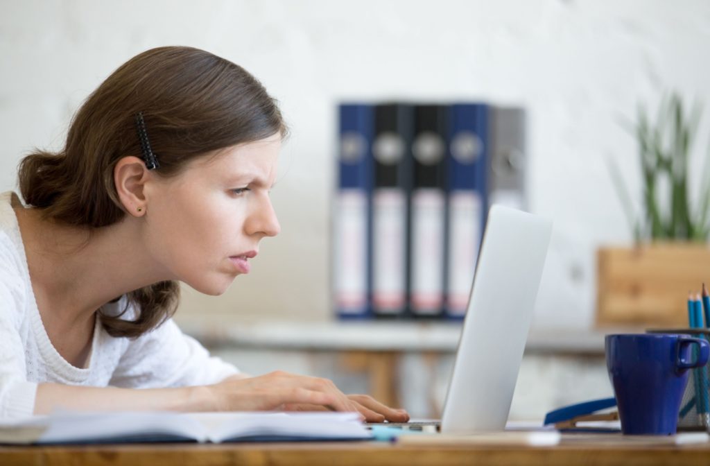 A woman squinting at her computer screen to see the content better.