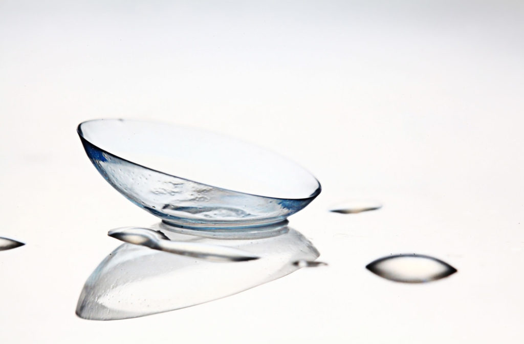 A contact lens sitting on a surface with contact lens solution droplets sitting around it.