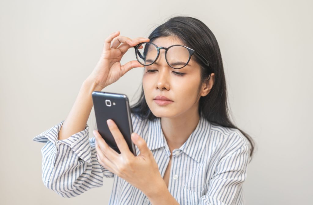 Woman lifting up her glasses and squinting at a phone screen.