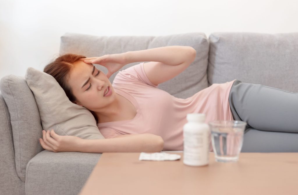 A woman laying on a couch holding her head in pain due to eye strain from eye tracking problems.