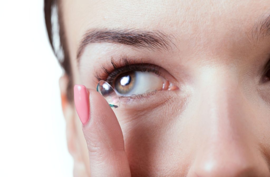 Close-up of a woman inserting a contact lens into her eye with her finger.