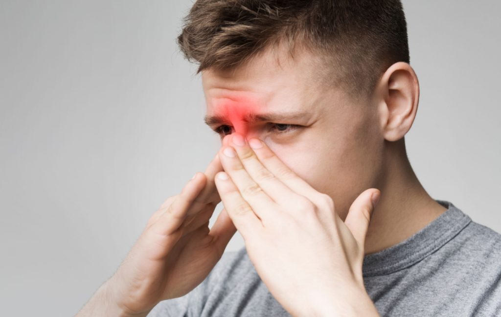 A person with sinusitis presses their hands to their sore face to try to relieve the pressure on their sinuses.