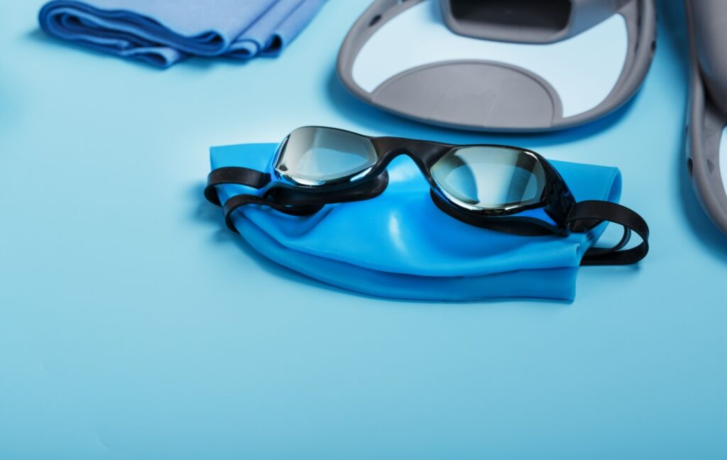A pair of prescription swim goggles sit on top of a bright blue swim cap before their wearer's swimming session.