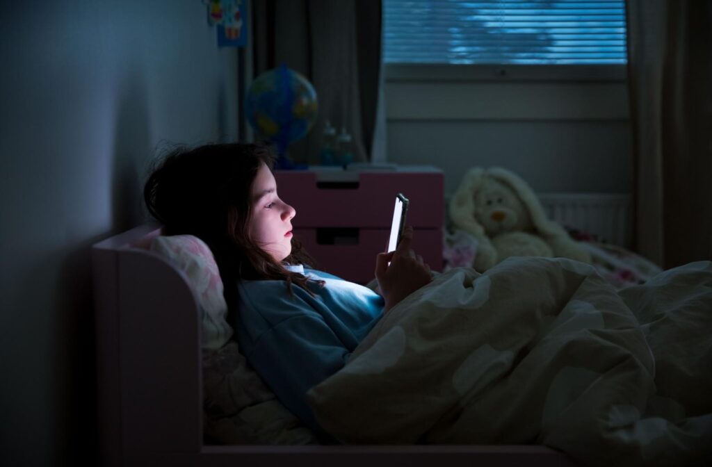 A young child staring at a phone screen in a darkly lit room.